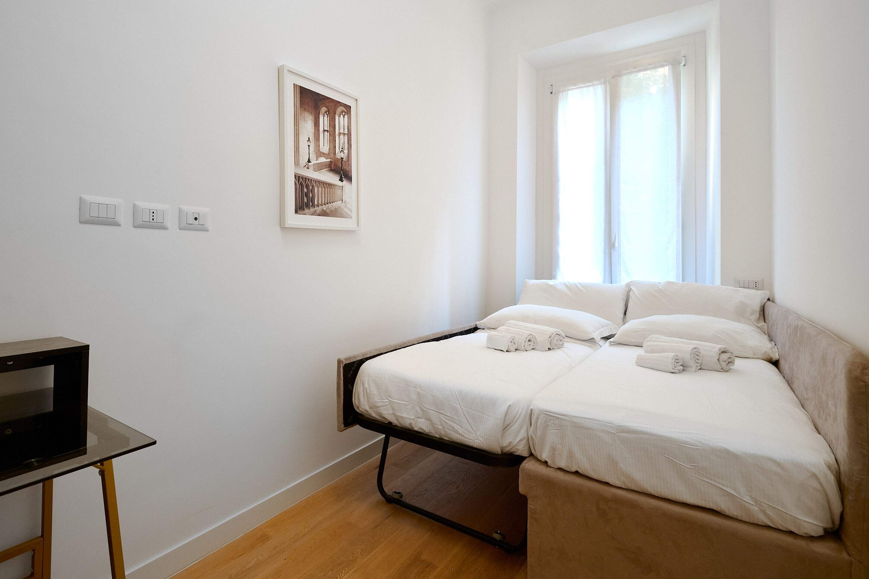 A bedroom with a bed, a desk, and a window.