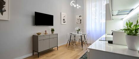Una cocina moderna con un televisor de pantalla plana, un comedor con una mesa redonda y sillas, y una planta en maceta sobre la encimera.