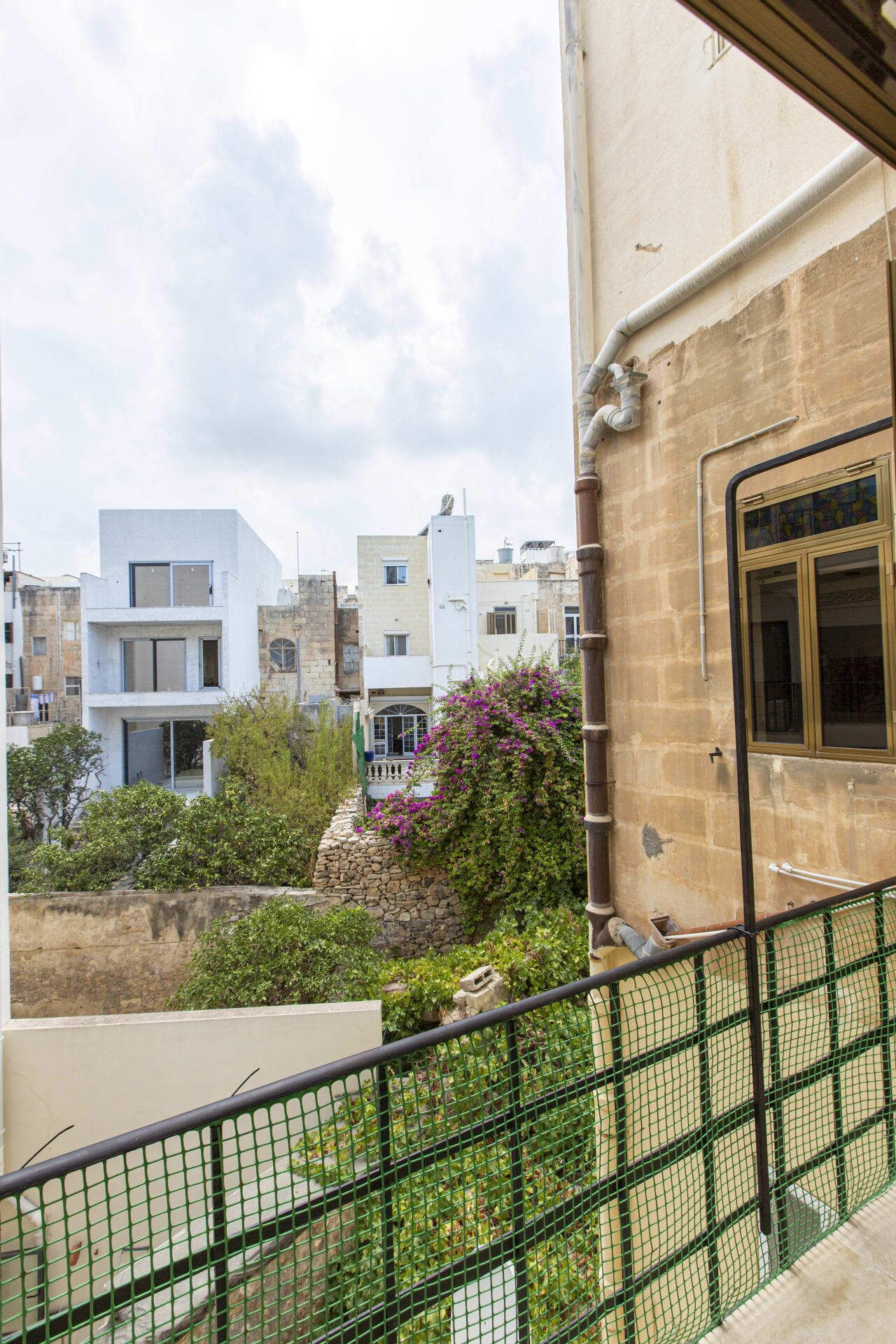 Un quartier résidentiel avec des immeubles modernes, un mur en pierre et un balcon doté d’une rambarde de sécurité verte.