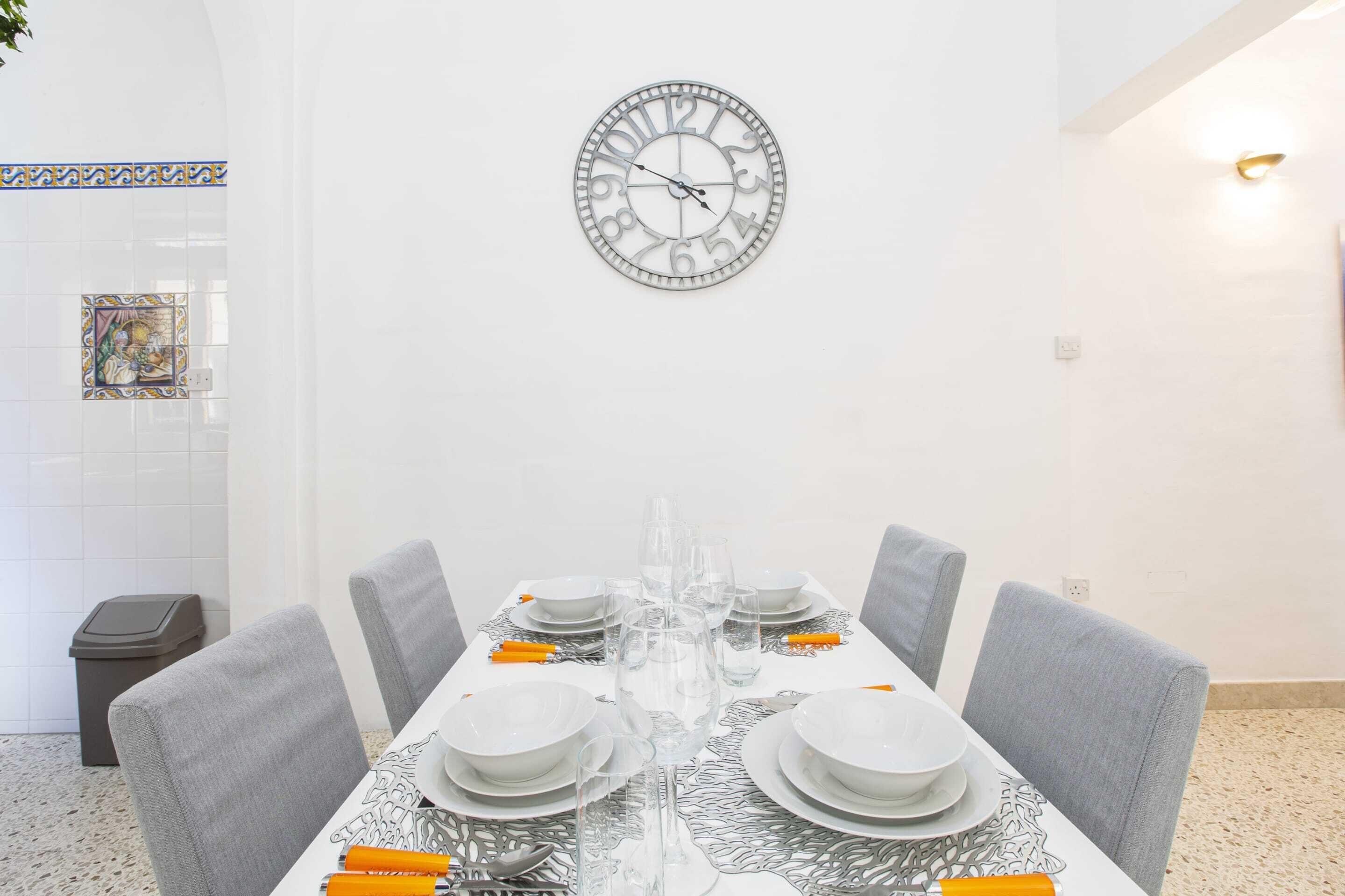 A dining area with a round wall clock, white tiled walls, and a tiled floor.