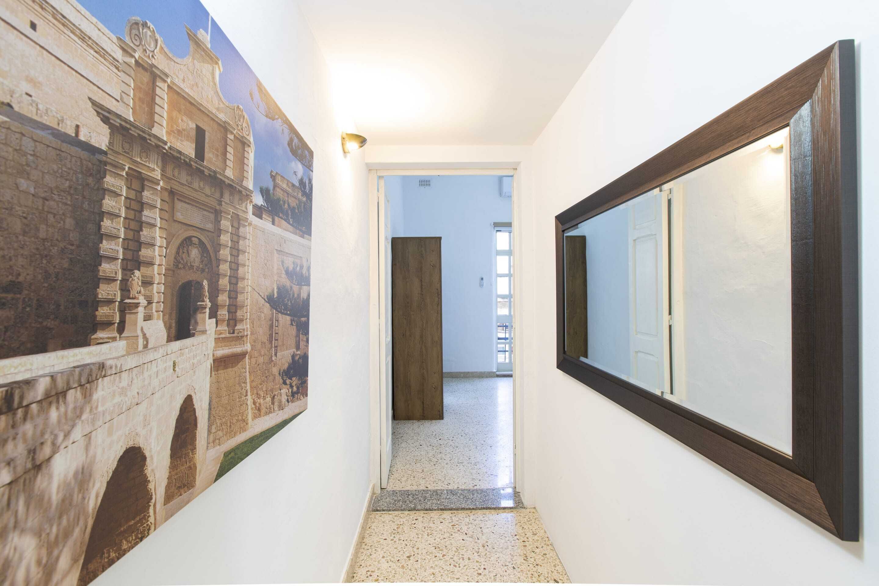 A hallway with a large mural of a historical building, a wooden door, and a mirror with a dark frame.