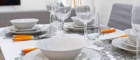 Una mesa de comedor dispuesta con platos blancos, tazones y copas de vino transparentes, con mangos anaranjados en los cubiertos.
