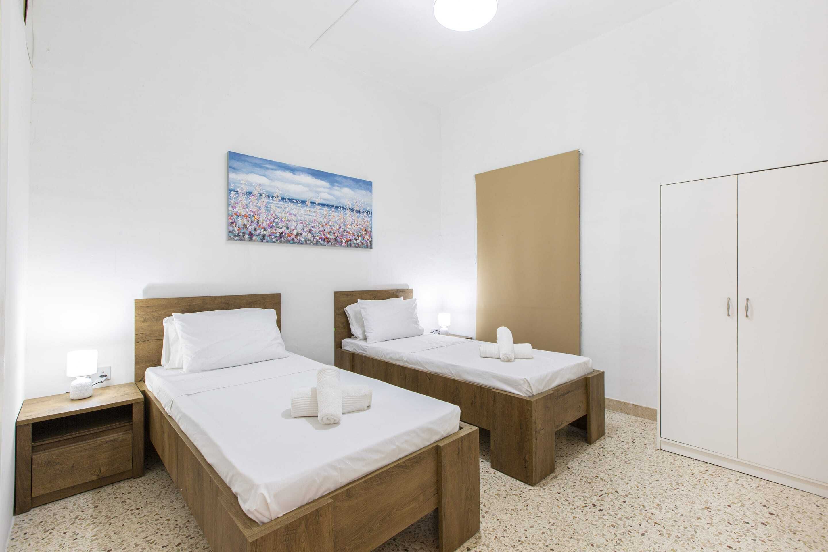A hotel room with two wooden beds, a large wardrobe, and a painting on the wall.