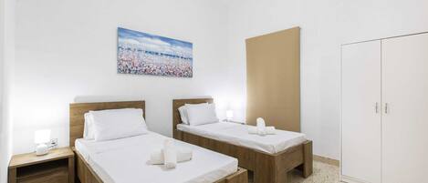 A hotel room with two wooden beds, a large wardrobe, and a painting on the wall.