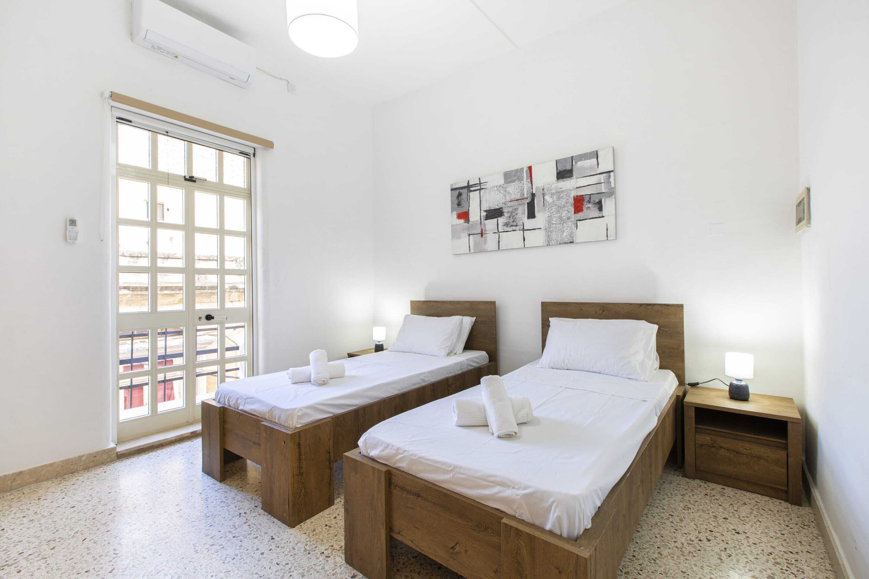 A room with two wooden beds, a door with a view, and a wall-mounted abstract art piece.