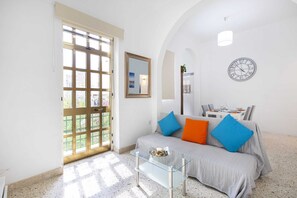A living room with a sofa, a glass coffee table, a wall clock, and a door leading to an outdoor area. - Sliema Lovely Flat (Sliema)