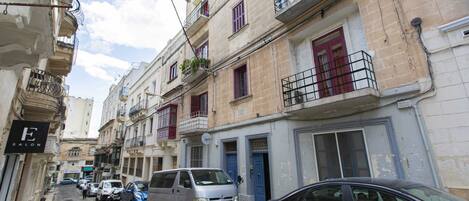 Una calle estrecha flanqueada por edificios de varios pisos, algunos con balcones y otros con tiendas a nivel de calle.