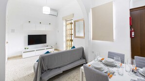 A modern living room with a sofa, TV, and dining area with table set for four. - Sliema Lovely Flat (Sliema)