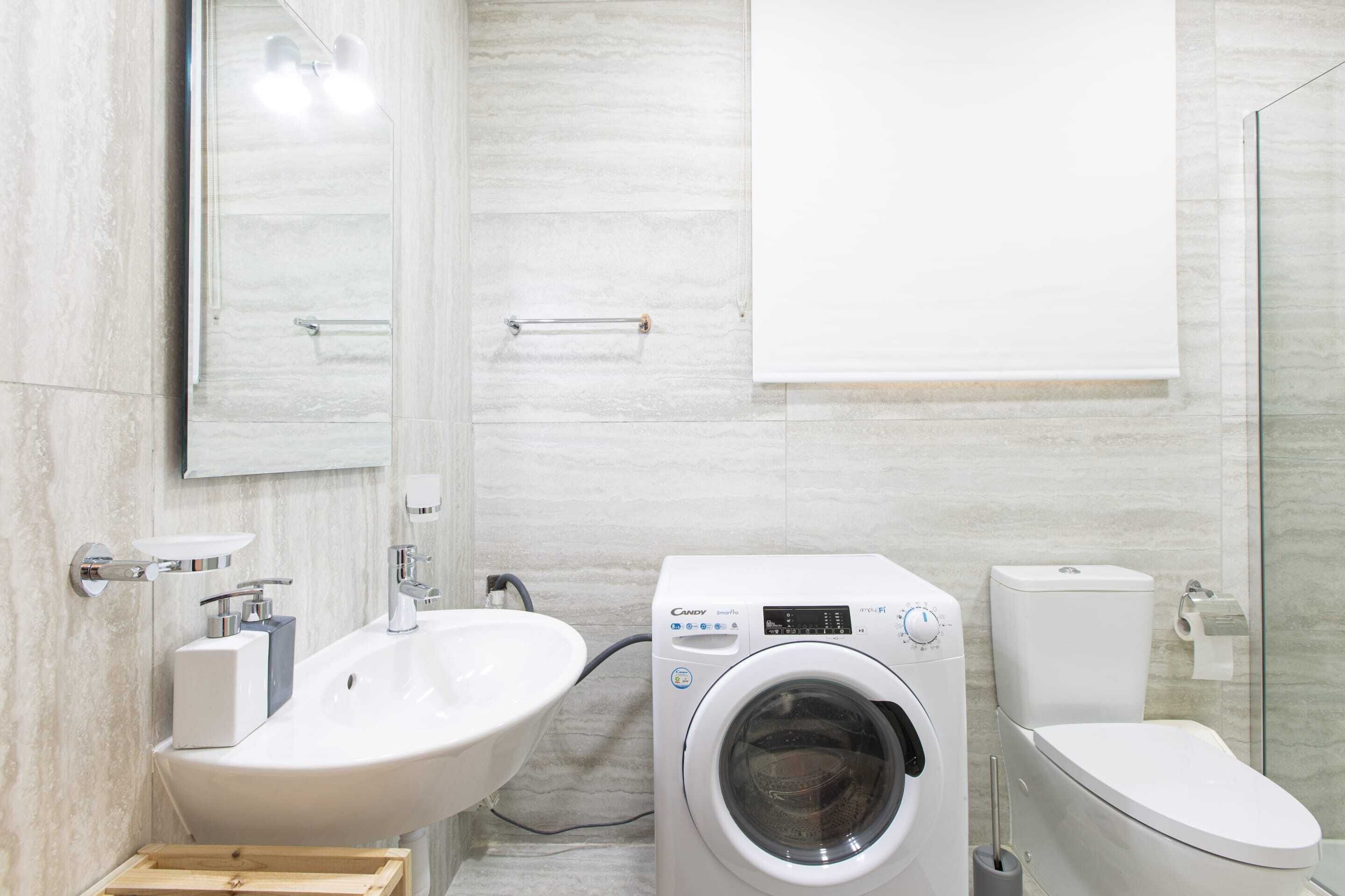 A modern bathroom with a sink, washing machine, and toilet.
