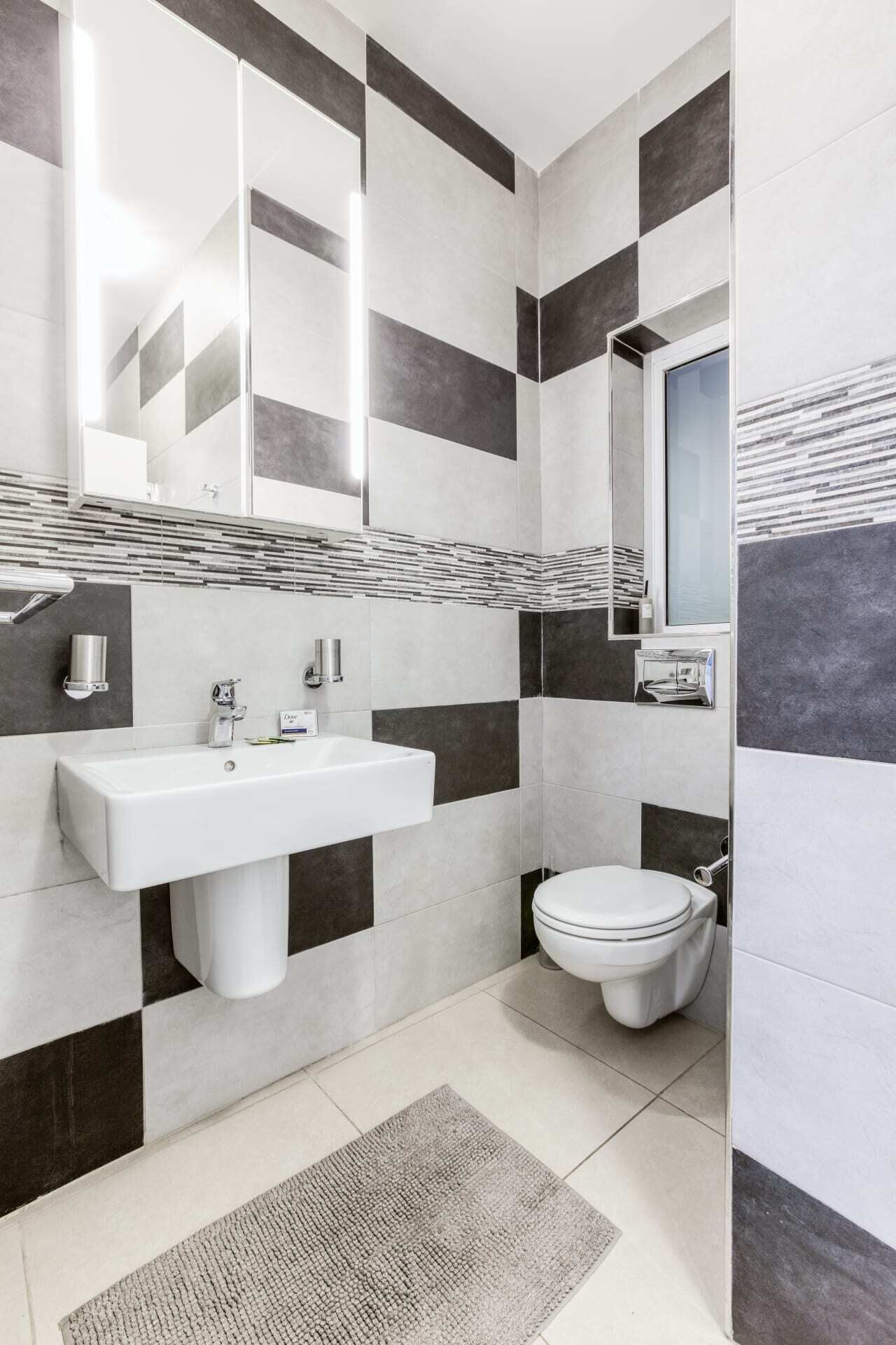 A modern bathroom with a white sink, a toilet, and a mirror. The walls have a black and white checkered pattern.