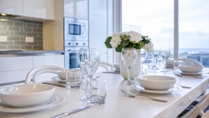 A modern kitchen with white cabinets, a large window, and a dining table set with white dishes and glasses. - Pool Penthouse (Swieqi)