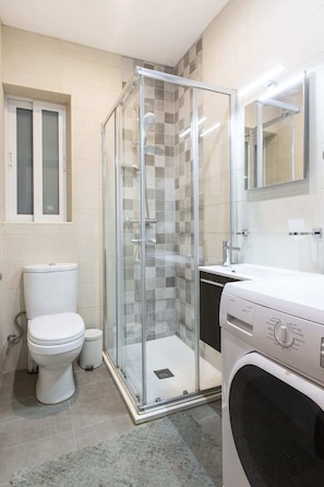 A bathroom with a glass-enclosed shower, a toilet, a washing machine, and a sink.