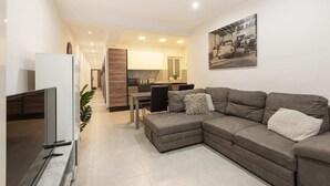 A modern living room with a sectional sofa, a flat-screen TV, and a dining area with a table and chairs. - Golden Flat in San Pawl (St. Paul's Bay)