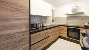 A modern kitchen with wooden cabinets, a built-in microwave, a stove, and a sink. - Golden Flat in San Pawl (St. Paul's Bay)