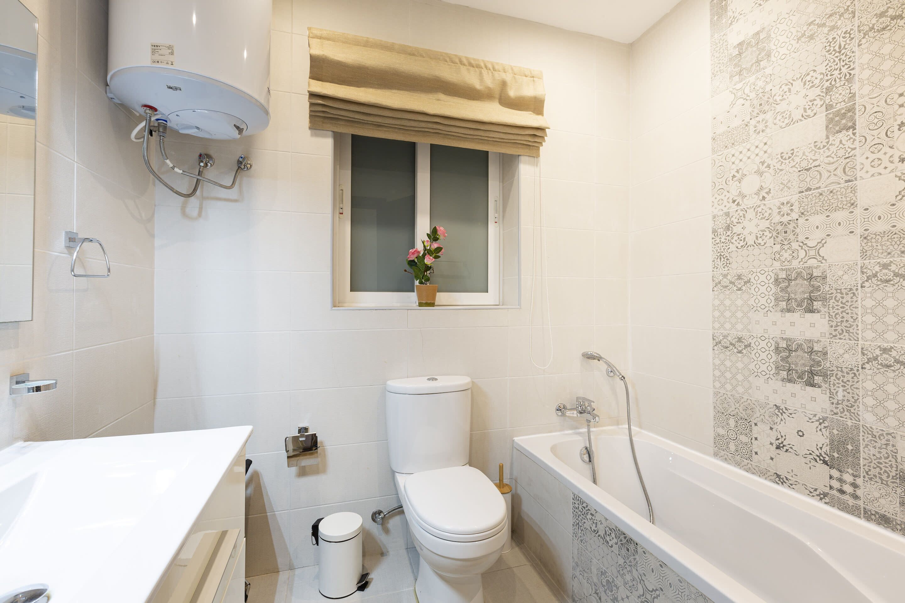 A bathroom with a toilet, sink, bathtub, and a window with a curtain.