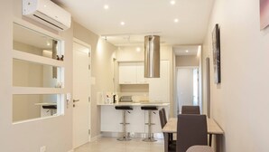 A modern kitchen with a central island, two bar stools, and a dining table with chairs. - Brand new 1BR in Central Malta (Pieta)