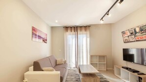 A modern living room with a sofa, coffee table, TV, and artwork on the walls. - Brand new 1BR in Central Malta (Pieta)