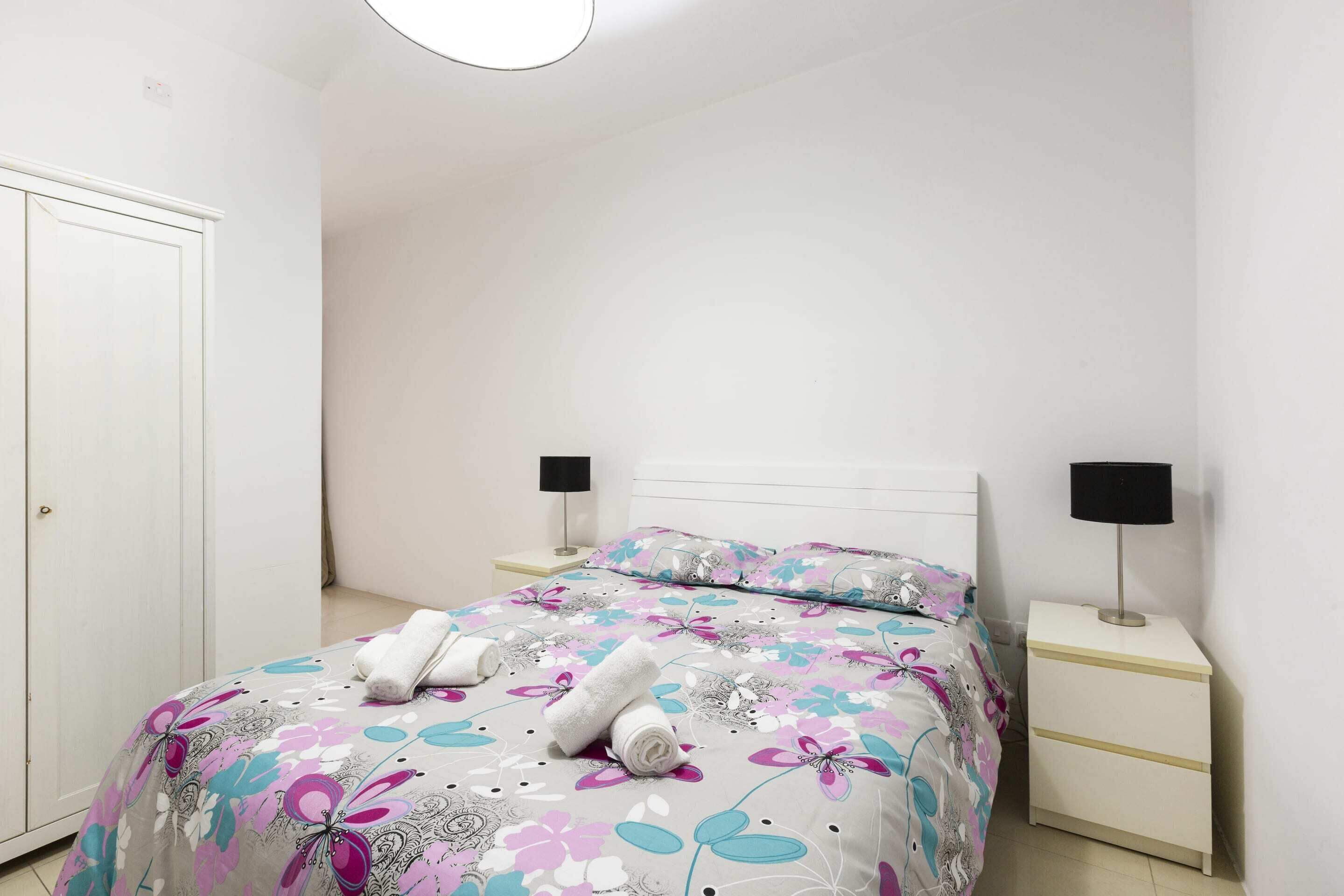 Een slaapkamer met een bed, twee nachtkastjes, een deur en een wandlamp.