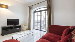 Una sala de estar moderna con un sofá rojo, una mesa de centro blanca, un televisor de pantalla plana sobre un mueble negro y un ventanal con cortinas.
