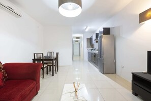 A modern living room with a red sofa, a dining area with chairs, a kitchen with stainless steel appliances, and a TV on a black stand. - Sliema 2 Bedroom Apartment (Sliema)