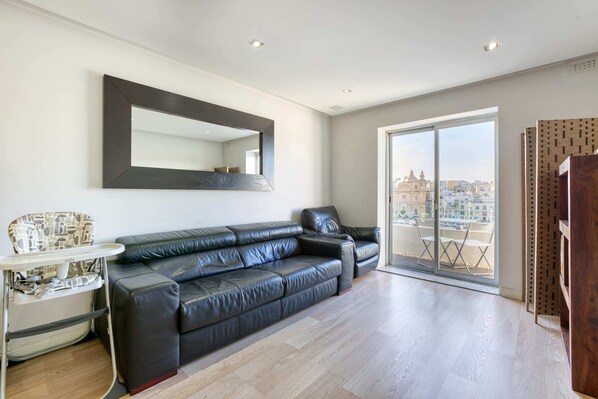 A modern living room with a black leather sofa, a white side table, and a large mirror on the wall. - Seafront Apartment (Pieta)