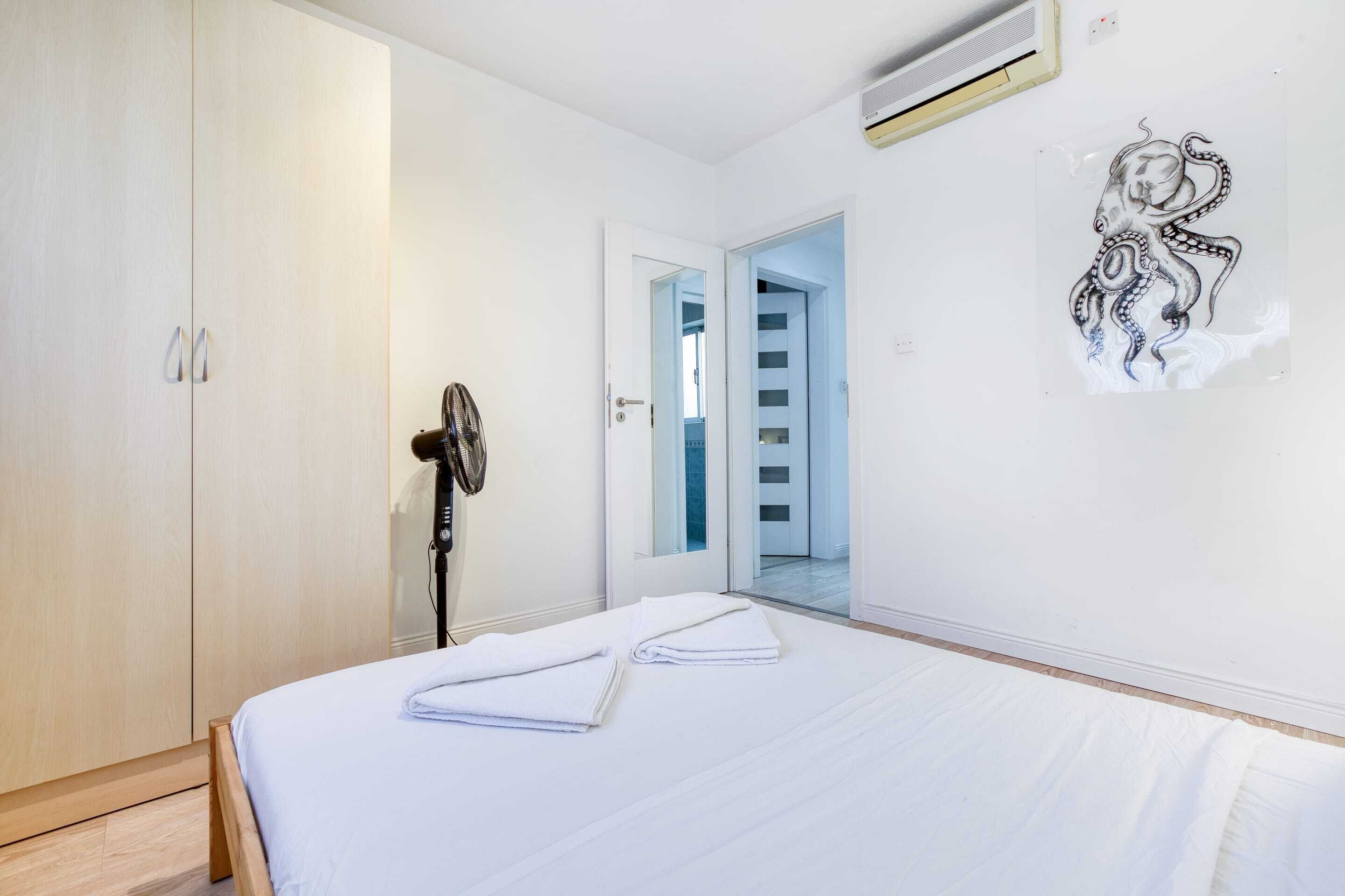 A bedroom with a bed, a wardrobe, a door leading to a staircase, and a wall-mounted air conditioner.