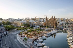 Un puerto deportivo con barcos amarrados, una carretera con vehículos, y un edificio histórico al fondo.