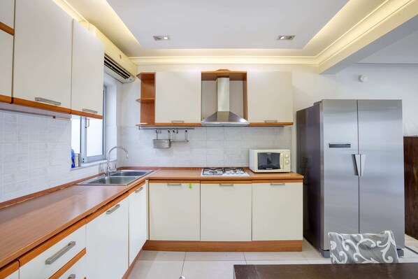 Una cocina moderna con armarios blancos, un refrigerador de acero inoxidable, un microondas y una estufa a gas.
