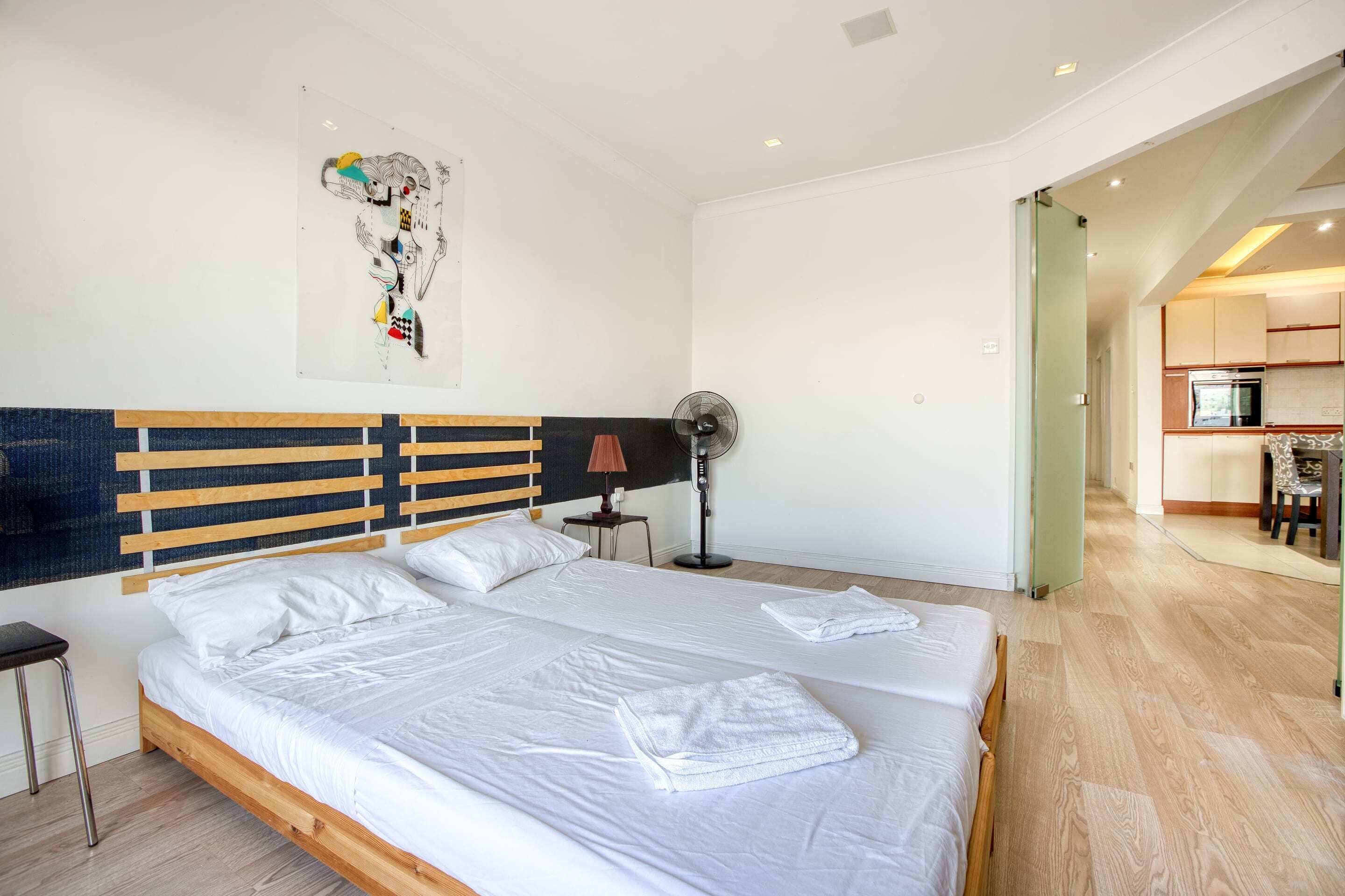 A modern hotel room with a large bed, a bedside table, a lamp, and a fan.