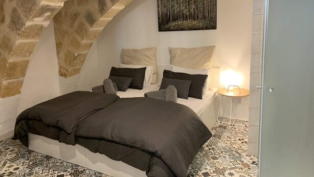 A bedroom with a stone arch, a bed with a dark cover, and a painting on the wall. - Valletta Studio (Valletta)
