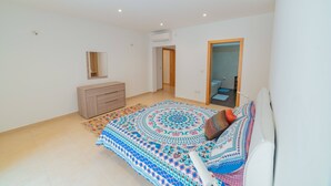 A bedroom with a large bed, a dresser, a mirror, and a door leading to another room. - Luxury Seaview & Pool (Mellieha)