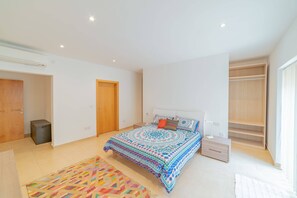 Quarto com cama grande, mesa de cabeceira, guarda-roupa e pequeno cesto de lixo.