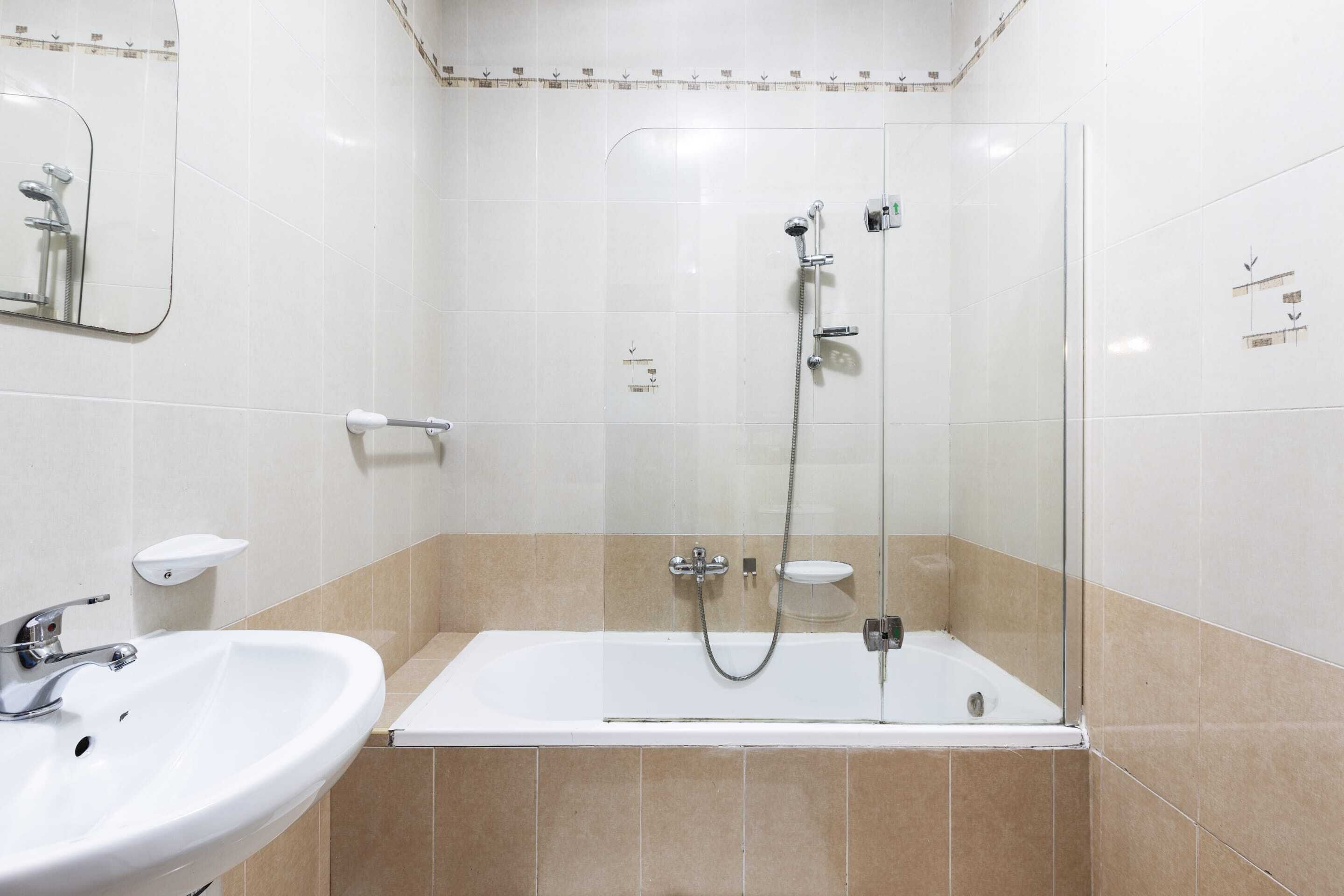 Une salle de bain moderne avec une douche à parois de verre, un lavabo blanc et des carreaux de couleur beige.