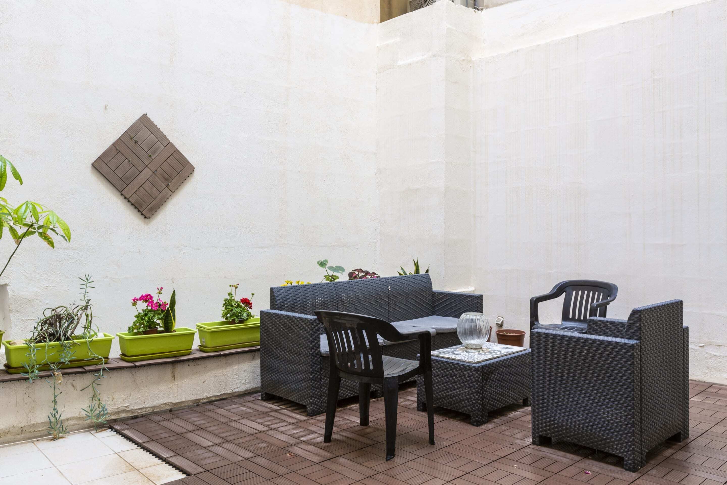 A patio area with a sofa, two chairs, a small table, and potted plants.