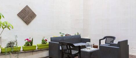 Un patio con un sofá, dos sillones, una mesita y plantas en macetas.