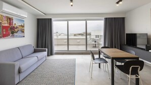 A modern living room with a grey sofa, a wooden dining table, and a TV. - Gzira Suite 13 (Gzira)