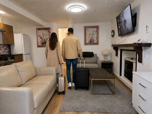 A living room with a sofa, a coffee table, a fireplace, a television, and a kitchen area with a refrigerator and stove. - Stylish Self-Catering Apartments (Liverpool)