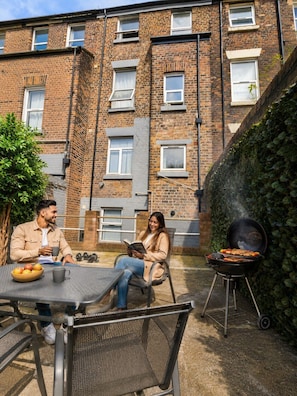A brick building with multiple windows, a barbecue grill, and a table with fruits and a book. - Stylish Self-Catering Apartments (Liverpool)
