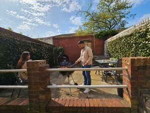 Une terrasse extérieure avec un mur en briques, un barbecue et une table avec des chaises.