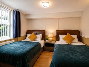 Une chambre d’hôtel avec deux lits, une table de chevet avec une lampe, une fenêtre avec des rideaux et un luminaire au plafond.
