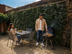 A patio with a table and chairs, a grill, and a brick wall with greenery. - Stylish Self-Catering Apartments (Liverpool)
