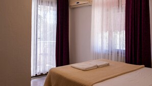 Hotellihuone, jossa on sänky, puinen penkki, kattovalaisin ja ilmastointilaite.