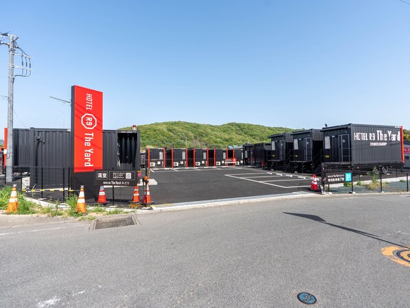 A hotel with a red sign, multiple black containers, and a parking area. - HOTEL R9 The Yard Midori (Midori)