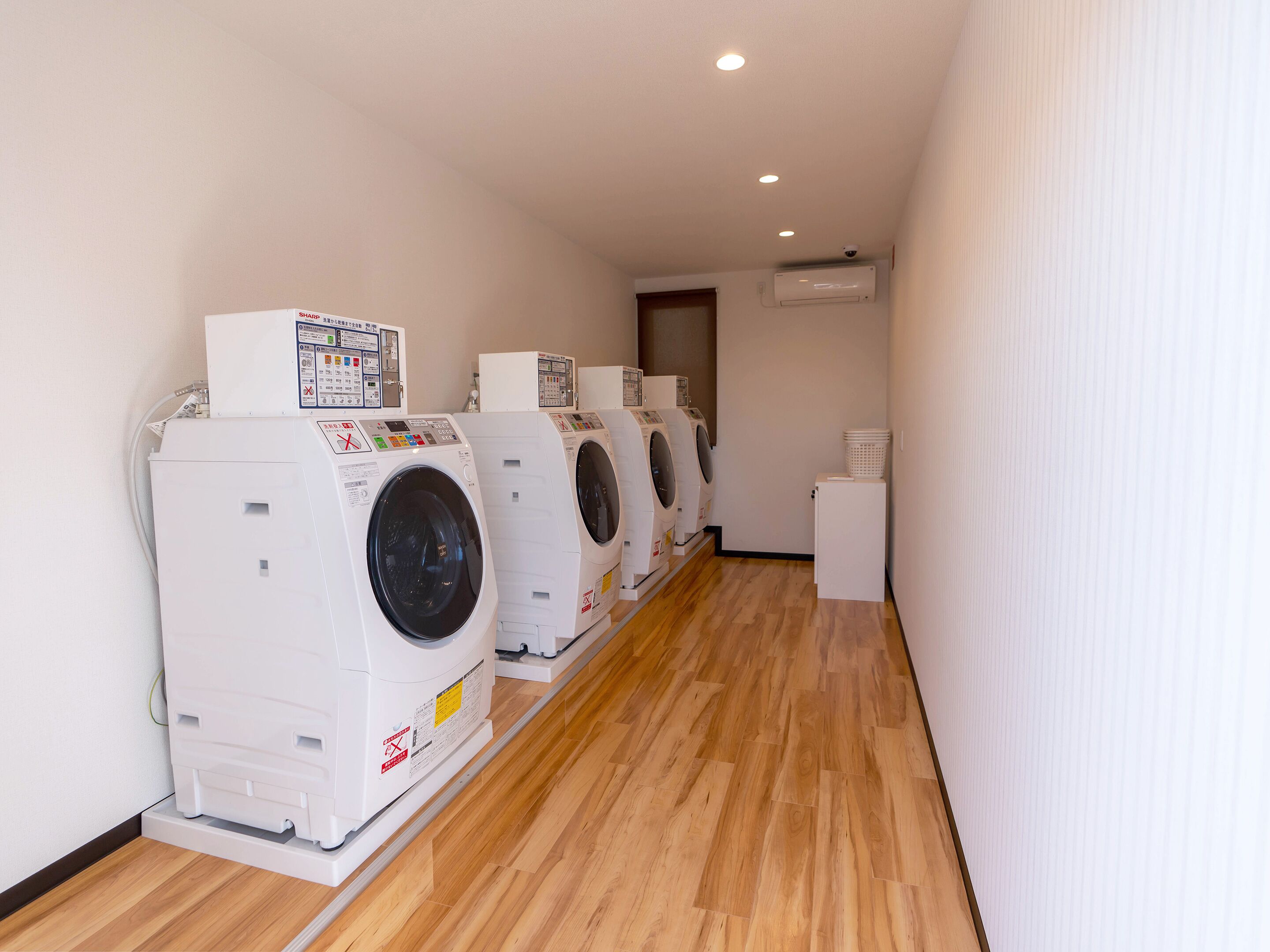 Una sala de bugaderia amb quatre rentadores frontals apilades i un refrigerador petit.