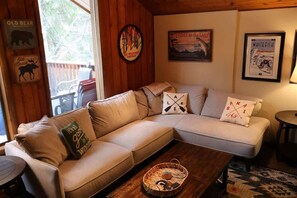 A cozy living room with a beige sectional sofa, a wooden coffee table, and a framed welcome sign.