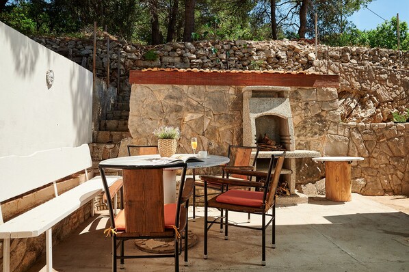 An outdoor patio with stone walls, a round table, wooden chairs, and a bench.