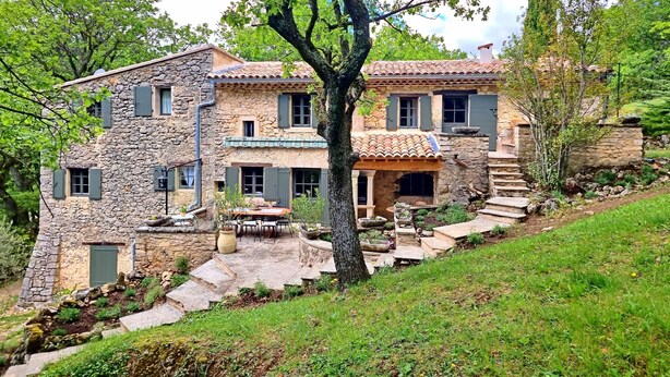 Una casa de piedra con tejado de tejas, una escalera de piedra y un patio amueblado con mobiliario exterior.