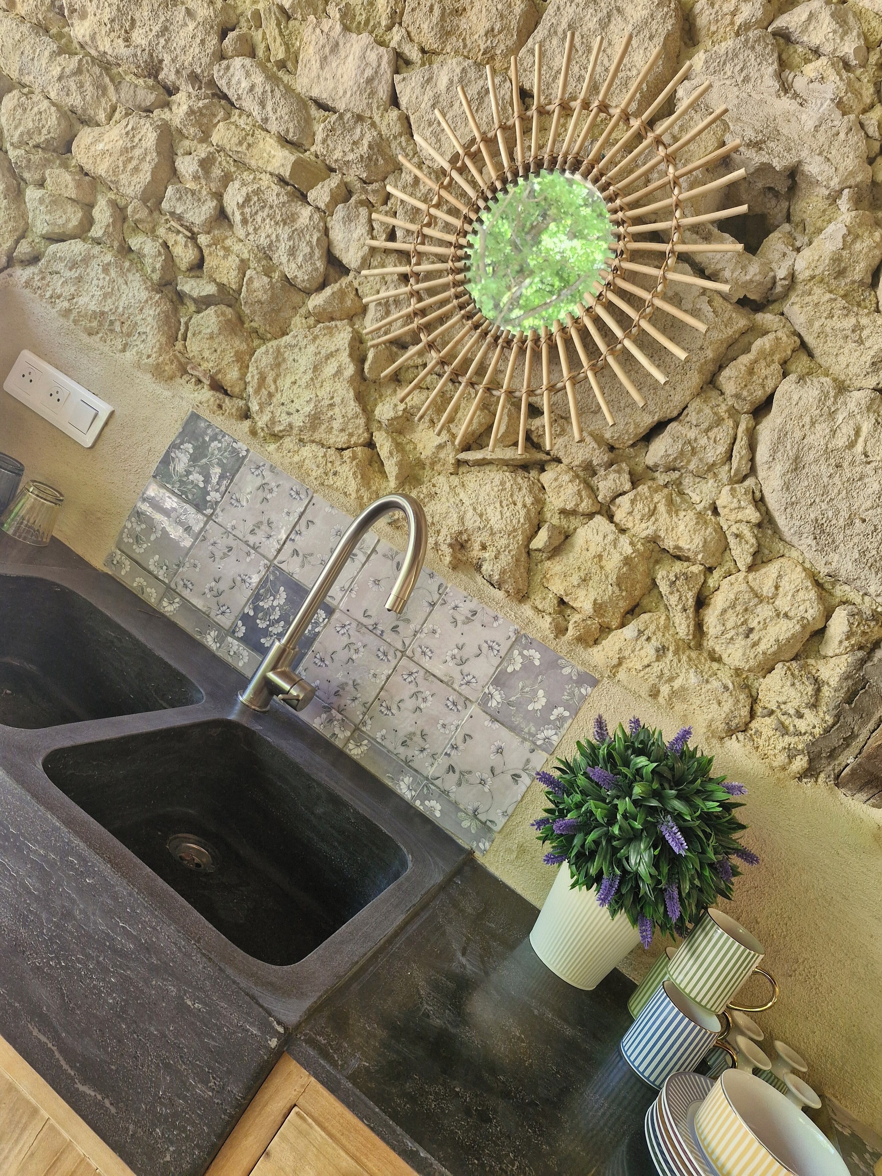 Cuina amb taulell de granat, un rentaplat i una paret decorativa amb un dibuix similar al sol, i una planta en test.