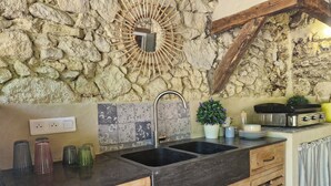 Una cocina con pared de piedra, un lavamanos negro, armarios de madera y salpicadero de azulejos.