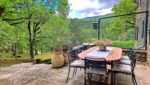 Un patio al aire libre con una mesa redonda y sillas, rodeado de plantas en macetas y un muro de piedra.